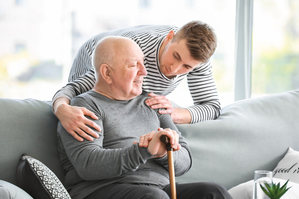 Young man leans over elderly man from behind a couch