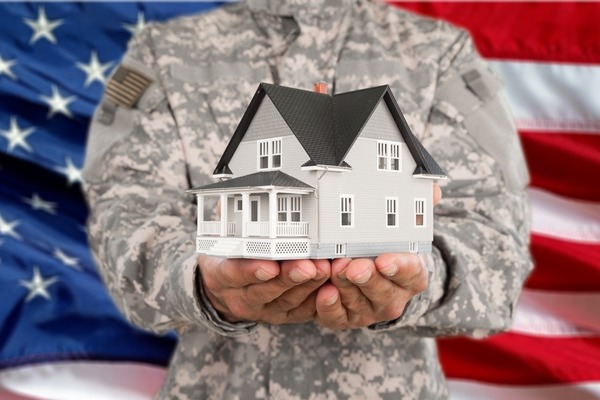 person in military uniform holding a model home